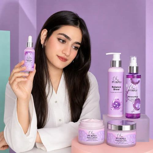 A woman in a white blouse holds up a purple skincare dropper bottle from Oh So Purple while several matching Oh So Purple products stand on display against a lavender studio background.