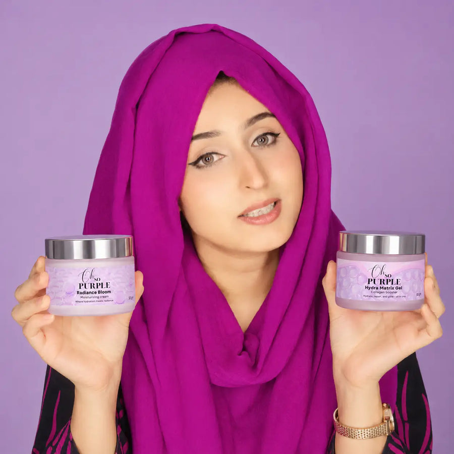 A woman wearing a bright magenta hijab holds two jars of 'Clear Purple' Hyaluhydrates Balancing Balm, one in each hand, against a solid lavender-purple background.